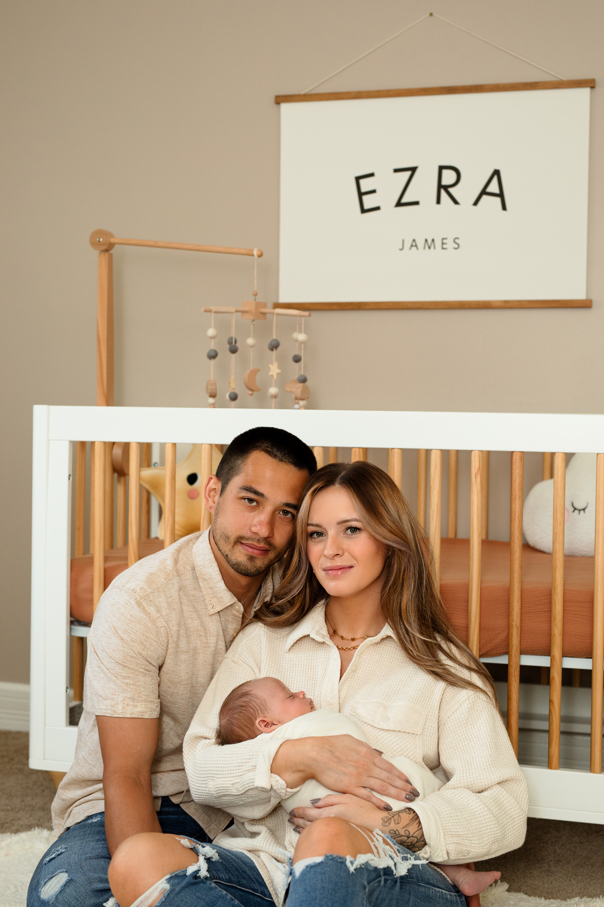 Mom and dad leaning against the crib, holding baby Ezra