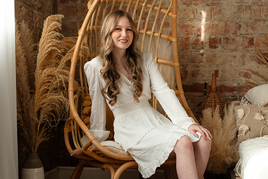 a teenage girl in a white dress, sitting in a rattan chair