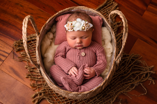 newborn baby girl in pink pajamas laying in a basket